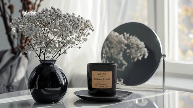 Mała świeca zapachowa z drewnianym knotem YLANG YLANG & RÓŻA sn82-000-384 Valpe przedstawiona obok eleganckich dekoracji wnętrzarskich. Dekoracyjna świeca doskonale komponuje się z nowoczesnym wystrojem salonu lub sypialni.