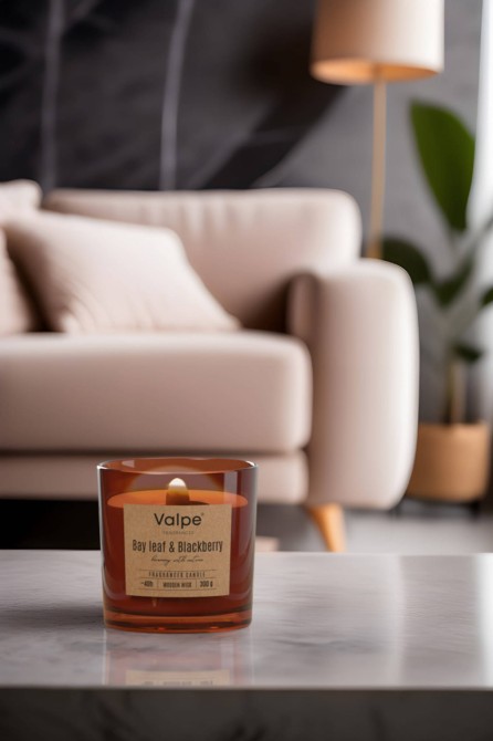 Świeca zapachowa z drewnianym knotem CEDARWOOD & VANILLA sn100-095-81 Valpe ustawiona przy sofie.