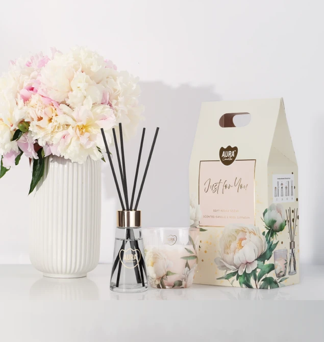 Zestaw zapachowy Aura Candles Just for You w aranżacji wnętrza. Świeca zapachowa w szkle z motywem piwonii oraz dyfuzor zapachowy z patyczkami  i doniczką z kwiatami tworzą elegancką dekorację i wprowadzają do pomieszczenia delikatny zapach.