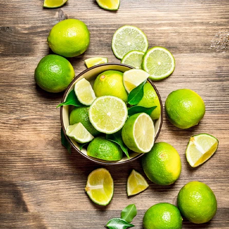 Na zdjęciu drewniany blat, a na nim miska pełna cytrusów limonek i cytryn. 
